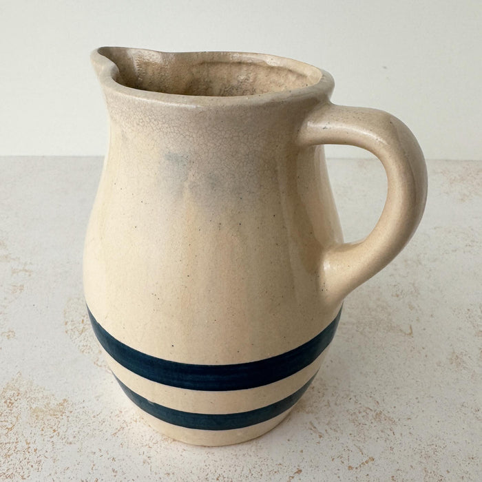 Side view of vintage beige stoneware pitcher showing rounded body, cobalt blue bands, spout, and handle