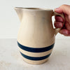 Hand holding vintage stoneware pitcher with cobalt blue bands