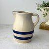 Vintage beige stoneware pitcher with two cobalt blue bands, rounded body, pouring spout, and loop handle