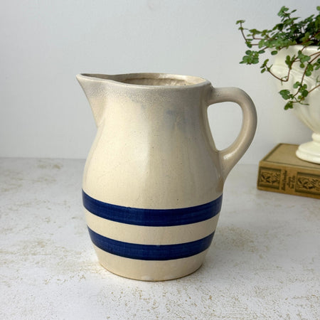 Vintage beige stoneware pitcher with two cobalt blue bands, rounded body, pouring spout, and loop handle