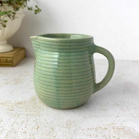 Small vintage Monmouth Pottery stoneware pitcher with ribbed body and soft green glaze styled with trailing plant