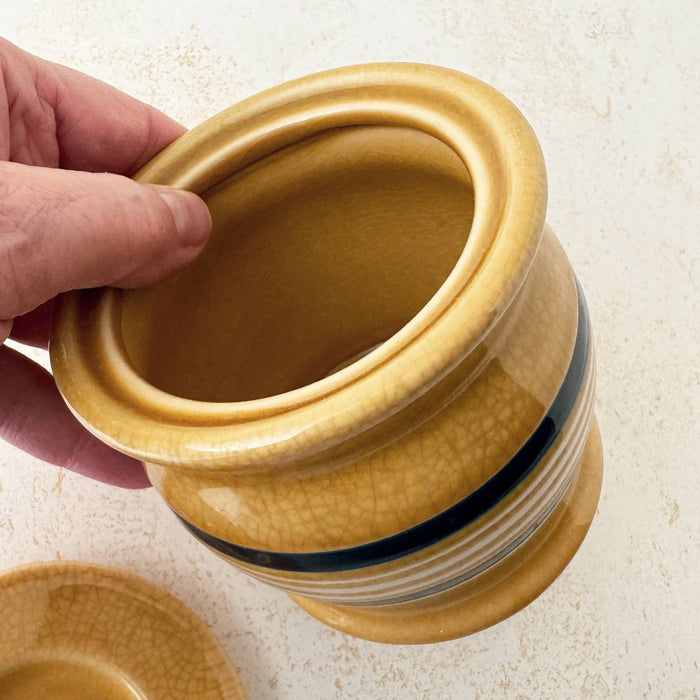 Hand holding rim of Park Designs yellowware canister