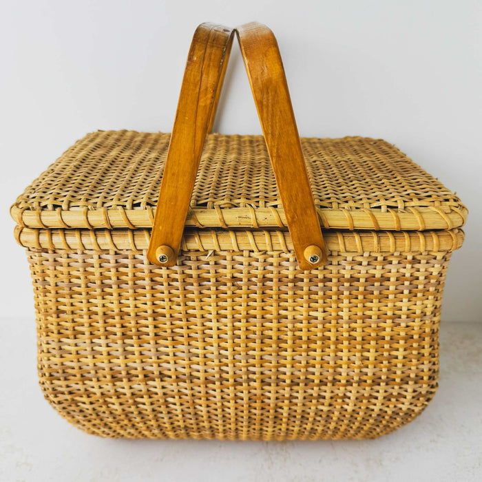 Side view of vintage lidded bamboo picnic basket with handles raised