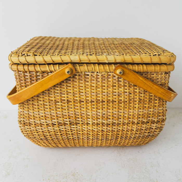 Side view of vintage lidded bamboo picnic basket with handles lowered