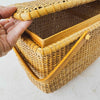 Angled three-quarter view of vintage lidded bamboo picnic basket with hand lifting lid