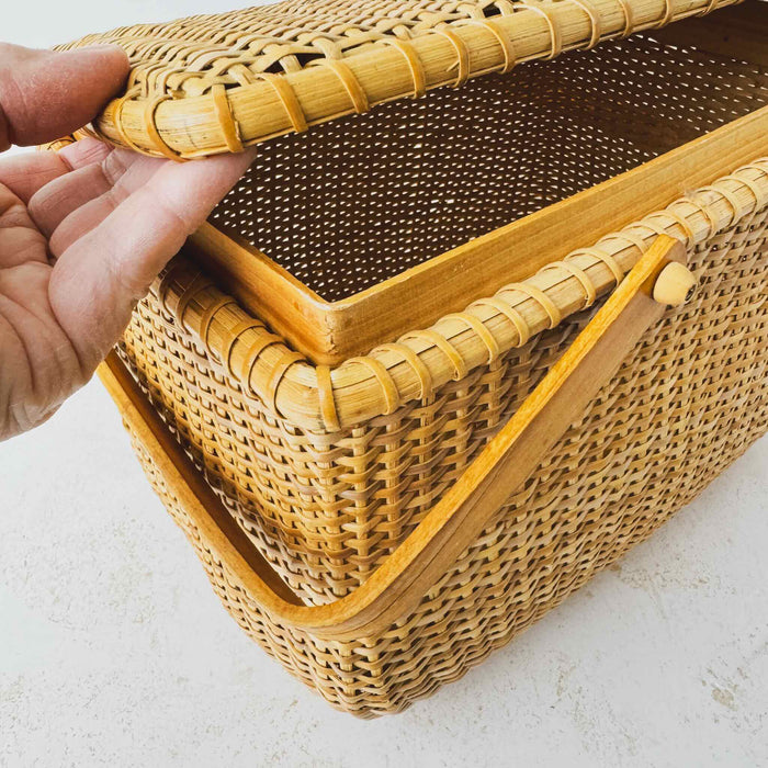 Angled three-quarter view of vintage lidded bamboo picnic basket with hand lifting lid