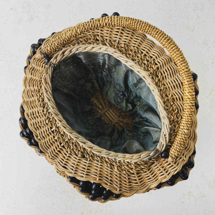 Top down view showing opening and fabric closure draped inside antique wicker vanity basket with beaded hexagonal form