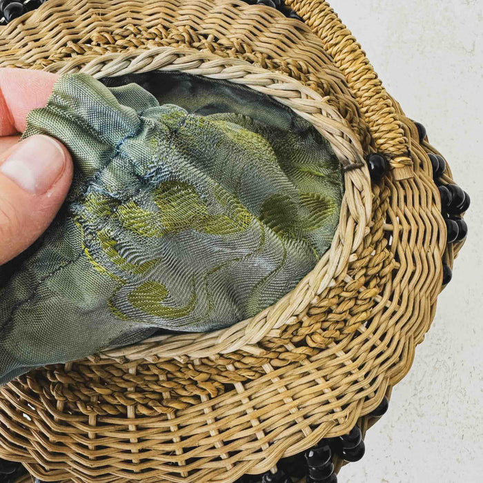 Hand holding fabric on antique wicker vanity basket with beaded hexagonal form