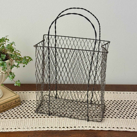 Vintage handwired wire basket with twisted handles and aged patina, styled empty on a crochet runner with antique book and trailing plant