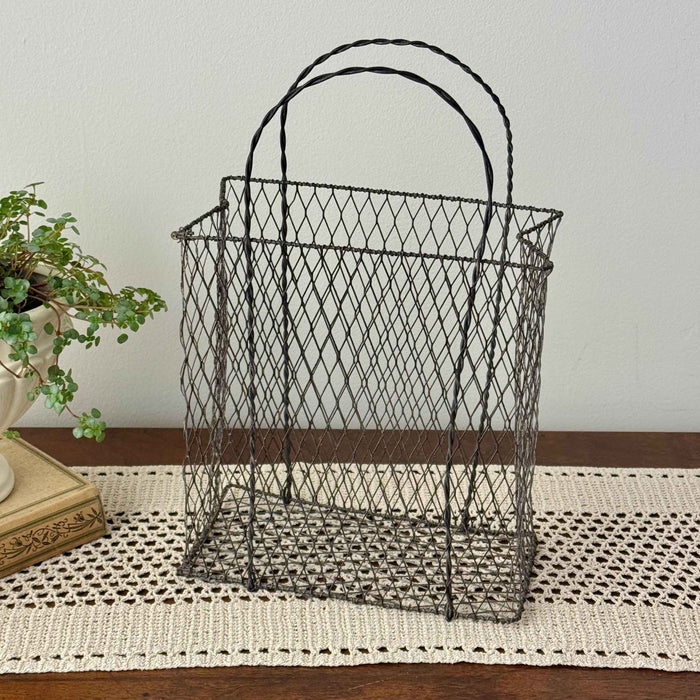 Vintage handwired wire basket with twisted handles and aged patina, styled empty on a crochet runner with antique book and trailing plant
