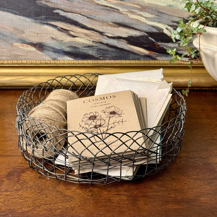 Vintage round wire basket used for organizing seed packets, garden notes, and twine on a wooden tabletop