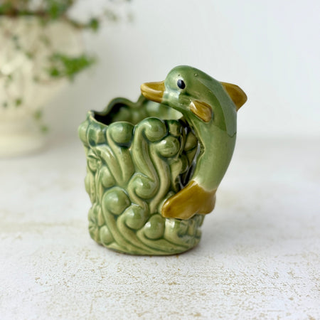 Vintage green ceramic planter with a figural dolphin arcing over sculpted waves and a scalloped rim