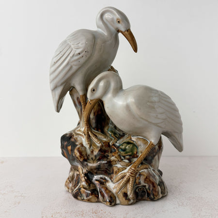 Vintage glazed earthenware spill vase with two white cranes on a naturalistic tree trunk base, majolica-style glaze in pooling browns, cream, and green