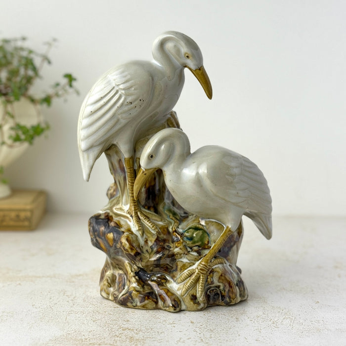 Vintage crane figural spill vase with two white glazed birds, amber beaks and legs, and a mottled brown, cream, and green majolica-style base