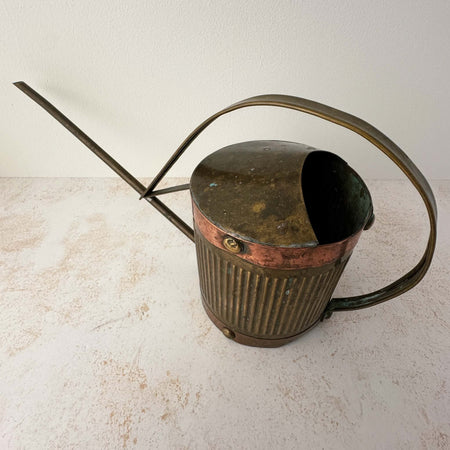 Angled three-quarter view of vintage brass indoor watering can with copper accents
