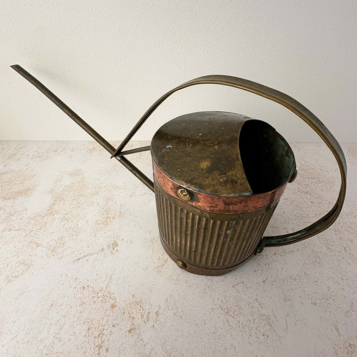 Angled three-quarter view of vintage brass indoor watering can with copper accents