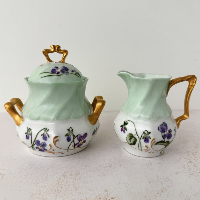 Side-by-side view of Jean Pouyat Limoges violets lidded sugar and creamer