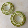 Top-down view of two Noritake Marlene Green tea trios showing teacups, saucers, side plates, floral details, green borders, and gold trim