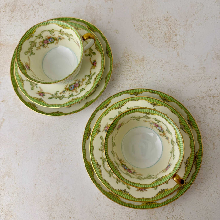 Top-down view of two Noritake Marlene Green tea trios showing teacups, saucers, side plates, floral details, green borders, and gold trim