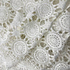 Close view of white crochet table runner loosely gathered in folds, showing repeating circular medallions, openwork connections, and scalloped border.