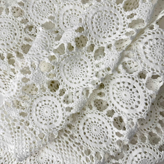 Close view of white crochet table runner loosely gathered in folds, showing repeating circular medallions, openwork connections, and scalloped border.