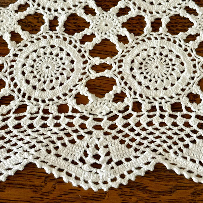 Close-up of white crochet table runner over dark wood, showing large circular medallions, smaller connecting motifs, openwork, and scalloped border.