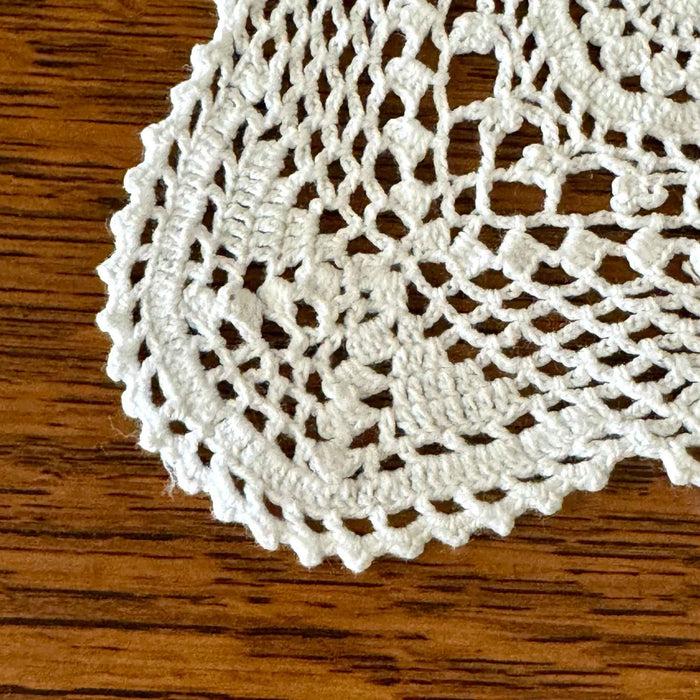 Close-up of a scalloped corner of the white crochet table runner, showing the openwork border and circular medallion pattern against dark wood.