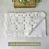Folded white crochet table runner placed over white linen for color comparison, showing the white thread, circular medallions, and openwork pattern.
