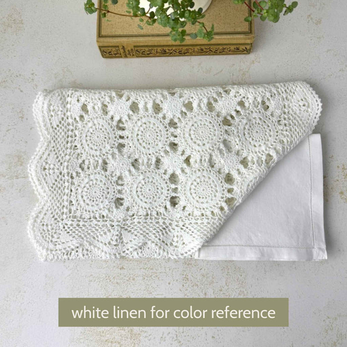 Folded white crochet table runner placed over white linen for color comparison, showing the white thread, circular medallions, and openwork pattern.