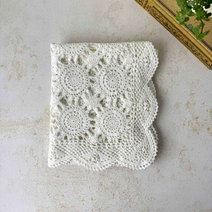 Overhead view of the neatly folded white crochet table runner, showing repeating circular medallions, openwork, and scalloped edges.