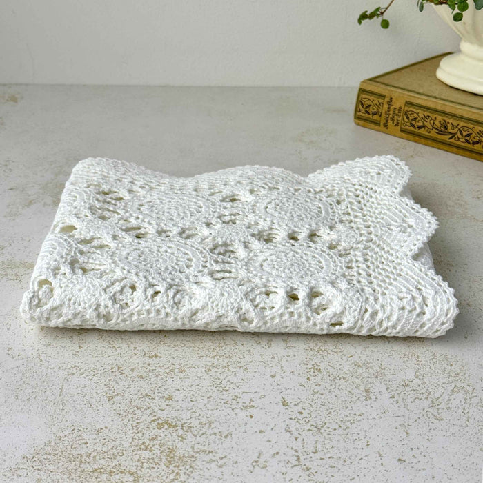 Low-angle view of the folded white crochet table runner showing its soft, flexible layers and openwork pattern.