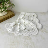 White crochet table runner loosely draped on a light surface, with soft folds showing the repeating circular medallions, openwork, and scalloped border.