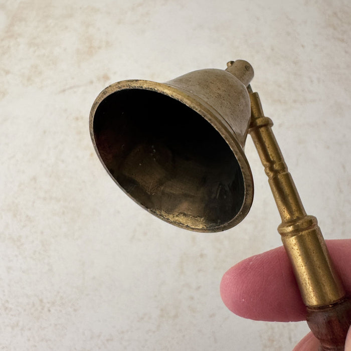 View of interior of vintage brass candle snuffer with turned wood handle held by a hand