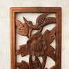 Close-up view of top of vintage hand-carved wooden panel showing bird and flower