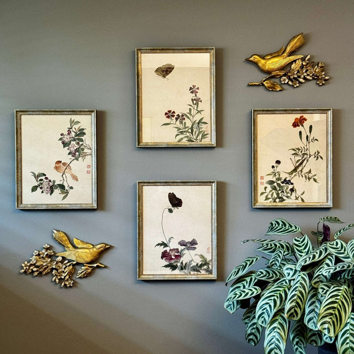 Pair of vintage gold bird wall plaques styled with framed botanical and insect artwork on a gray-green wall