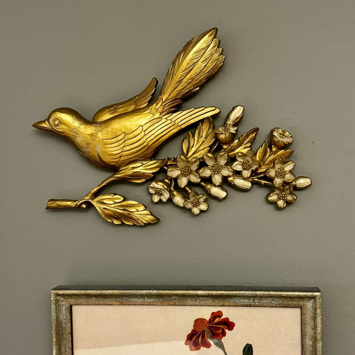 Vintage gold bird wall plaque styled above framed botanical art on a gray-green wall