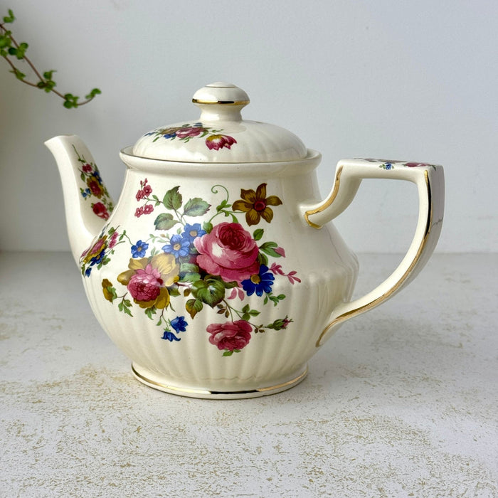 Angled front view of vintage Sadler floral teapot showing the ribbed cream body, curved spout, angular handle, and gold trim.