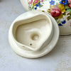 Underside of vintage Sadler teapot lid showing the cream-colored glazed interior, vent hole, and inner flange.