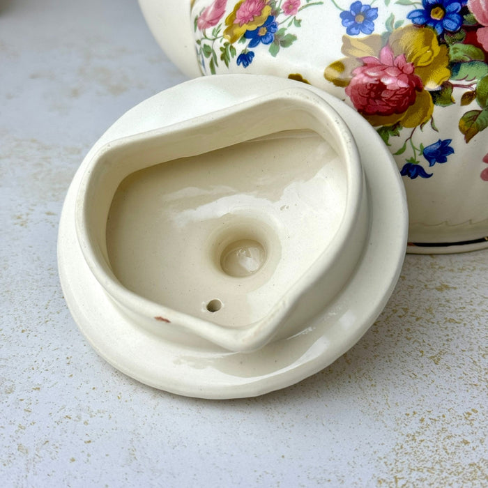 Underside of vintage Sadler teapot lid showing the cream-colored glazed interior, vent hole, and inner flange.