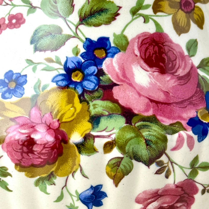 Close-up of the teapot’s colorful floral decoration with pink roses, blue flowers, golden-brown blossoms, and green leaves.