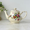 Vintage Sadler England teapot with pink, blue, and golden-brown floral bouquets, ribbed cream ceramic body, and gold trim.
