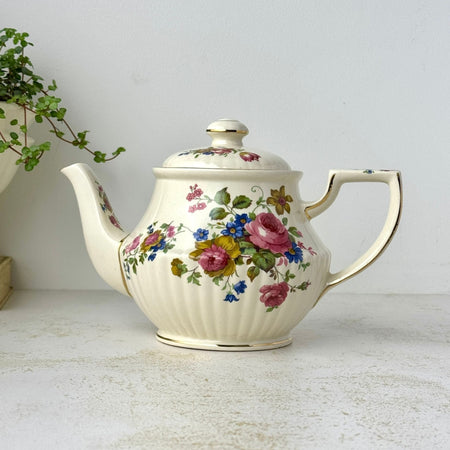 Vintage Sadler England teapot with pink, blue, and golden-brown floral bouquets, ribbed cream ceramic body, and gold trim.