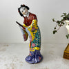 Vintage Chinese export porcelain figurine of a woman in a forward-inclined pose, holding a hand mirror, with robe painted in deep red, teal, yellow, and cobalt blue with pink peony motifs