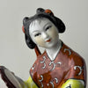 Close-up of hand-painted face on vintage Chinese porcelain woman figurine showing fine brushwork, arched brows, downcast eyes, and black sculpted hair