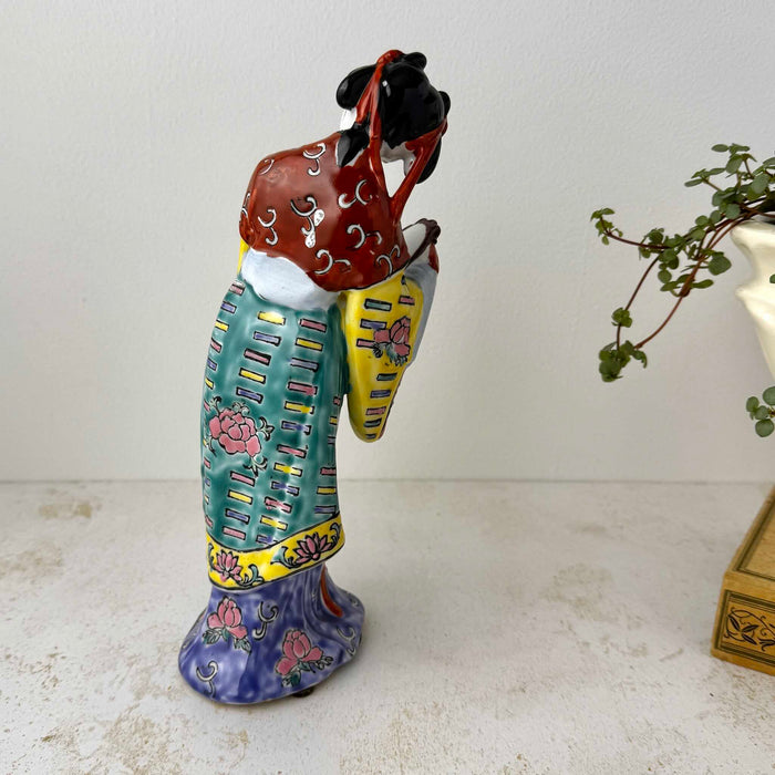 Rear three-quarter view of vintage Chinese porcelain court lady figurine showing the back of her robe and dangling red hair ribbons 