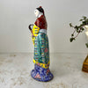 Opposite side view of vintage Chinese porcelain woman figurine showing yellow and teal robe panels and cobalt blue base with pink peony motifs