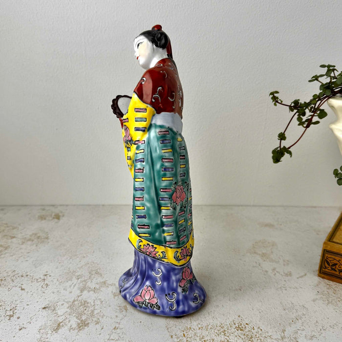 Opposite side view of vintage Chinese porcelain woman figurine showing yellow and teal robe panels and cobalt blue base with pink peony motifs