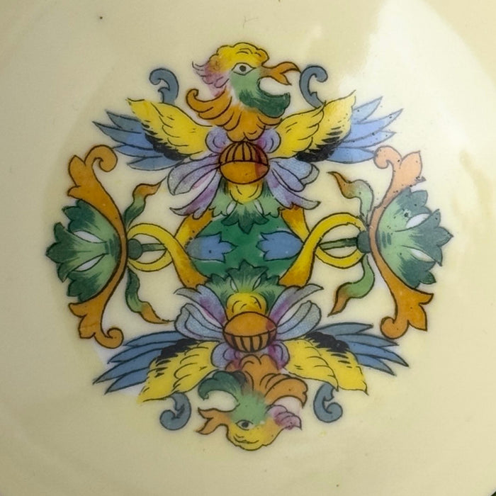 Close-up of the bowl's central decoration showing two stylized birds, yellow and blue wings, green foliage, lavender flowers, and gold-colored scrolling ornament.