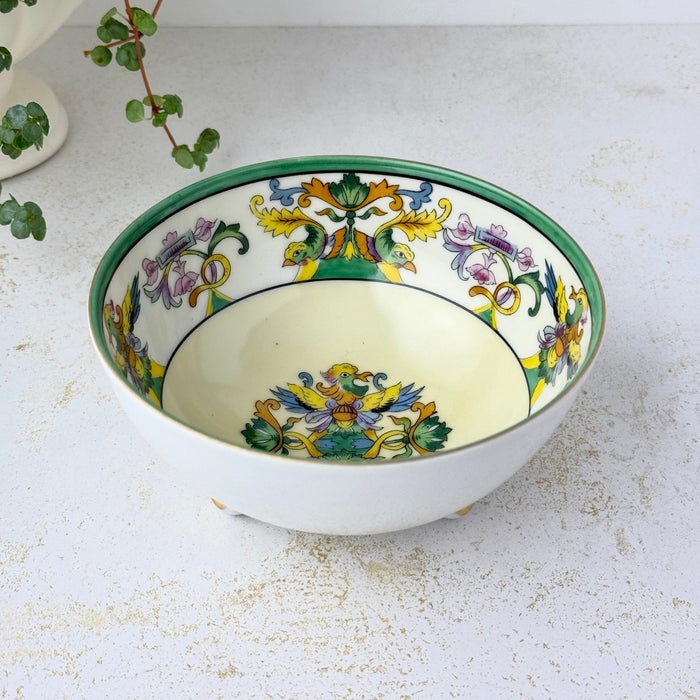Angled view of the porcelain bowl showing its green rim, cream interior, colorful bird and floral border, and central decoration.