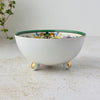 Side profile of the white porcelain bowl showing its rounded shape, green interior rim, and three ball feet with gilded accents.